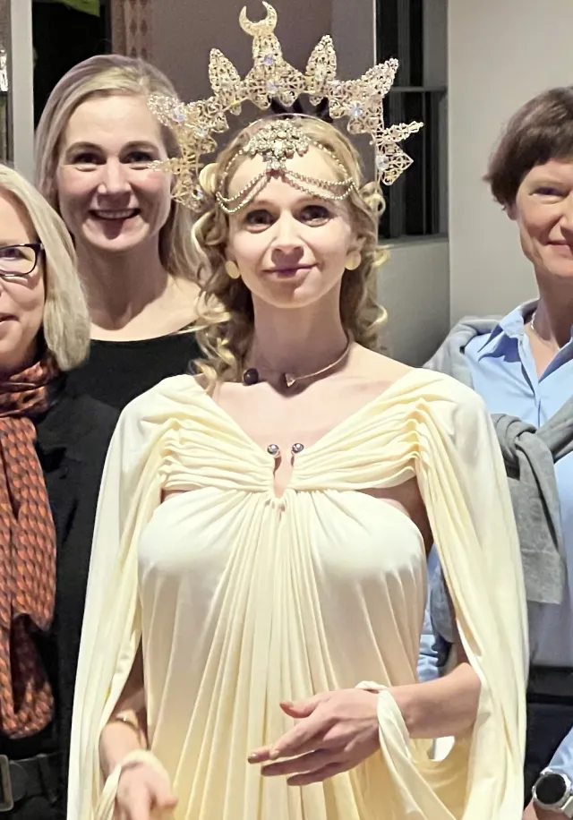 JUNO as BerliNike in a gilded gown with a glowing crown at a reception