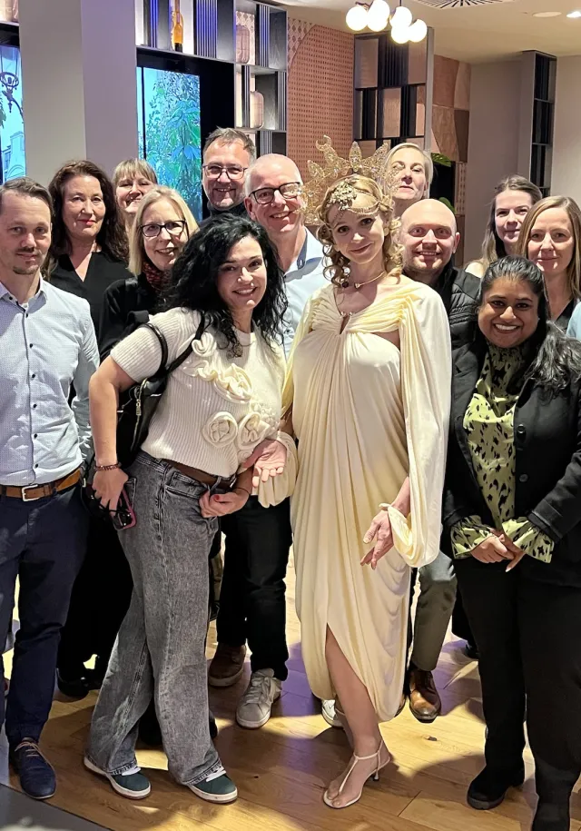 JUNO as BerliNike at a reception, surrounded by the guests of a corporate event